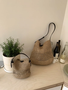 Detail of woven straw tote bags showing texture contrast and black leather straps