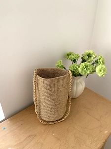 Détail de la texture d'un sac seau tissé avec fibres dorées et poignée tressée