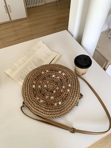 Detail of round straw crossbody bag with colorful beads and adjustable strap on a table
