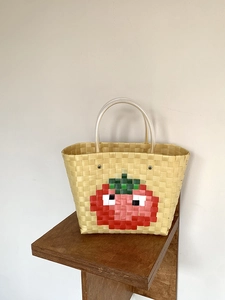 Detail of hand-woven plastic beach bag featuring red tomato pattern and clear handles