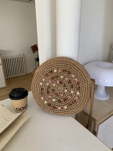 Detail of round straw bag with colorful beaded spiral pattern and leather shoulder strap