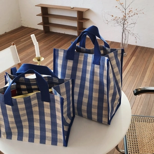 Detail of blue and white gingham canvas tote bag set on a minimalist white table