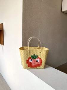 Detail of yellow woven beach tote bag with pixelated red tomato pattern and clear handles