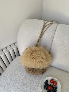 Detailansicht der Stroh-Eimertasche mit Tüll-Spitzenbesatz auf einem weichen Sofa