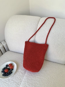 Détail d'un sac seau tissé rouge sur canapé blanc avec décor de fruits frais