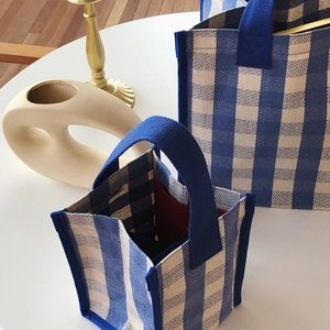 Detail of blue and white checkered canvas tote bags on a minimalist white desk setup