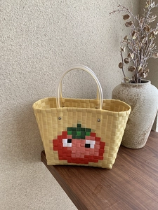 Handwoven yellow tote bag with pixel tomato pattern and transparent handles on wooden table