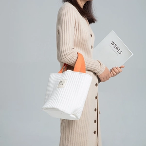 Détail du sac en toile matelassé blanc avec anses orange et écusson chat porté par le modèle