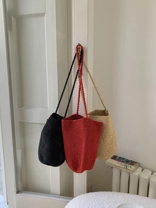 Sacs seau en paille tressée à la main en noir, rouge et beige suspendus à une porte