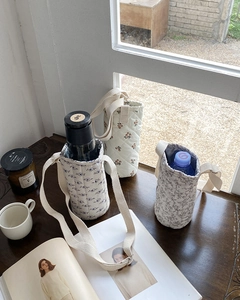 Quilted floral water bottle bags with adjustable cream straps on a sunlit wooden surface