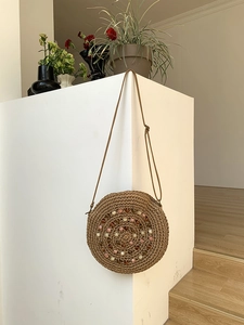 Detail of round straw bag with colorful spiral beadwork and slim leather shoulder strap