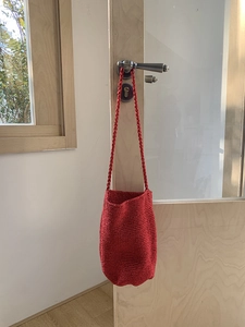 Détail du sac seau rouge tissé à la main avec texture crochet sur une porte en bois