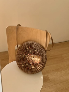 Detail of round straw bag with colorful beads and brown leather strap on chair