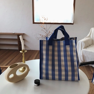 Close-up of blue and white checkered canvas tote bag on a minimalist white table