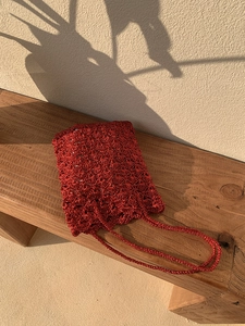 Close-up of red metallic knit crossbody bag with shell texture on a wooden bench
