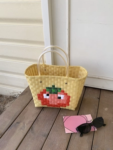 Detail of yellow woven basket bag featuring pixel tomato design and clear resin handles