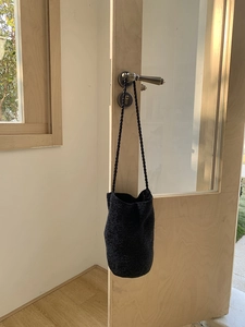 Gros plan d'un sac seau tressé noir suspendu à une poignée de porte en bois avec texture