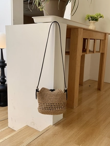 Detail of hand-woven hollow straw shoulder bag with sleek black strap and magnetic closure