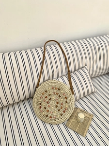 Detail of round straw bag with colorful bead accents and brown leather strap on a sofa