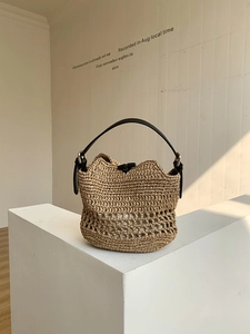 Handwoven straw beach bag with hollow mesh design and black leather handle on a white stand