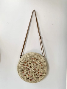 Detail of round straw bag with colorful bead embroidery and brown leather shoulder strap
