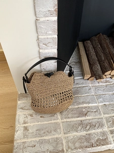 Detail of hand-woven straw beach bag with black leather handle and horn buckle closure