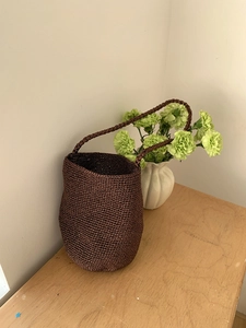Détail d'un sac seau tressé marron sur une table en bois avec un vase de fleurs vertes