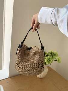 Detail of woven straw bucket bag with black leather handle and olive wood buckle closure