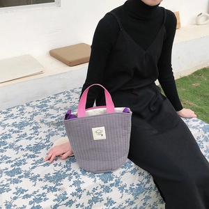Détail d'un sac en toile matelassé gris avec des poignées roses et emblème de mouton