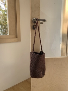 Détail d'un sac seau tressé marron foncé avec texture suspendu à une poignée en bois