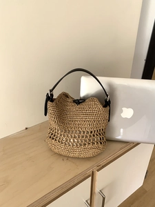 Detail of hollow woven straw bucket bag with black leather handle and metal hardware