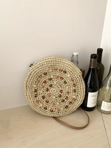Detail of round straw bag featuring spiral weave with colorful beads and leather strap