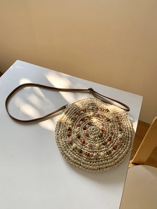 Detail of bohemian round straw bag featuring colorful beadwork and leather strap