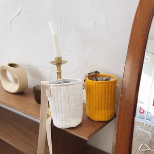Quilted water bottle carrier bags in white and ginger yellow on a wooden shelf