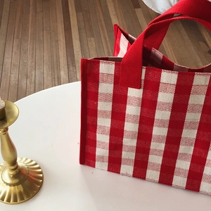 Detailed view of red and white checkered canvas tote bag on a white table with candle