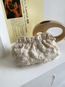 Detail of cream lace clutch bag with 3D floral textures and an elegant pearl pendant