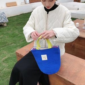 Sac seau matelassé bleu avec anses jaunes présenté dans un cadre extérieur naturel