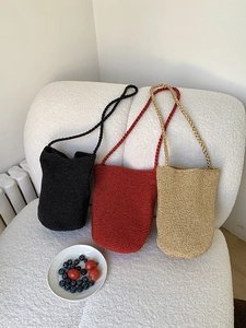 Sacs seaux en maille tissée à la main en noir, rouge et or sur un canapé à texture douce