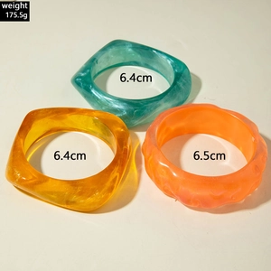 Close-up of chunky resin bangles in green, amber, and orange with translucent finish