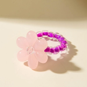 Detail of pink resin flower ring with purple beaded band on a beige surface