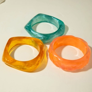 Detailed view of three translucent resin bangles in green, amber, and orange hues