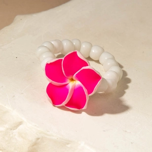 Macro detail of a beaded ring featuring a vibrant pink plumeria flower on a natural stone