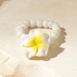 Close-up of tropical Plumeria flower beaded ring on a textured stone surface