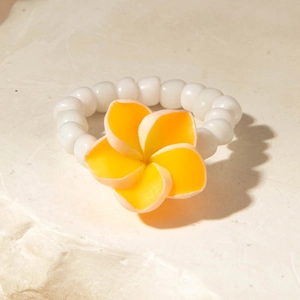 Detail view of a yellow plumeria flower bead ring on a natural stone base with shadows