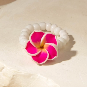 Close-up of a vibrant pink plumeria flower ring with white beads on a stone surface