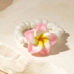 Macro detail of beaded flower ring with pink plumeria on natural stone background