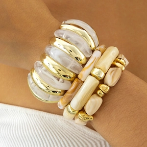 Detail of layered gold metal and marble resin beaded bracelets on a model wrist
