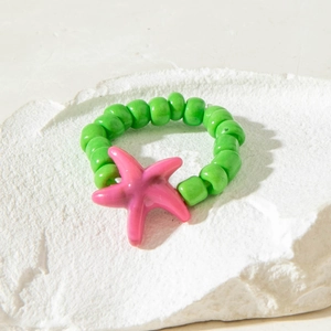 Detail view of light green beaded ring featuring a pink starfish charm on stone