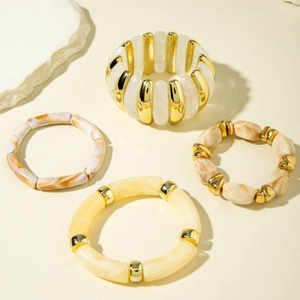 Detail of four acrylic beaded bracelets in gold and marble tones on a beige surface