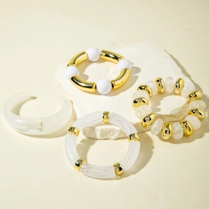 Detail of stacked acrylic beaded bracelets and gold bangles on a natural stone surface